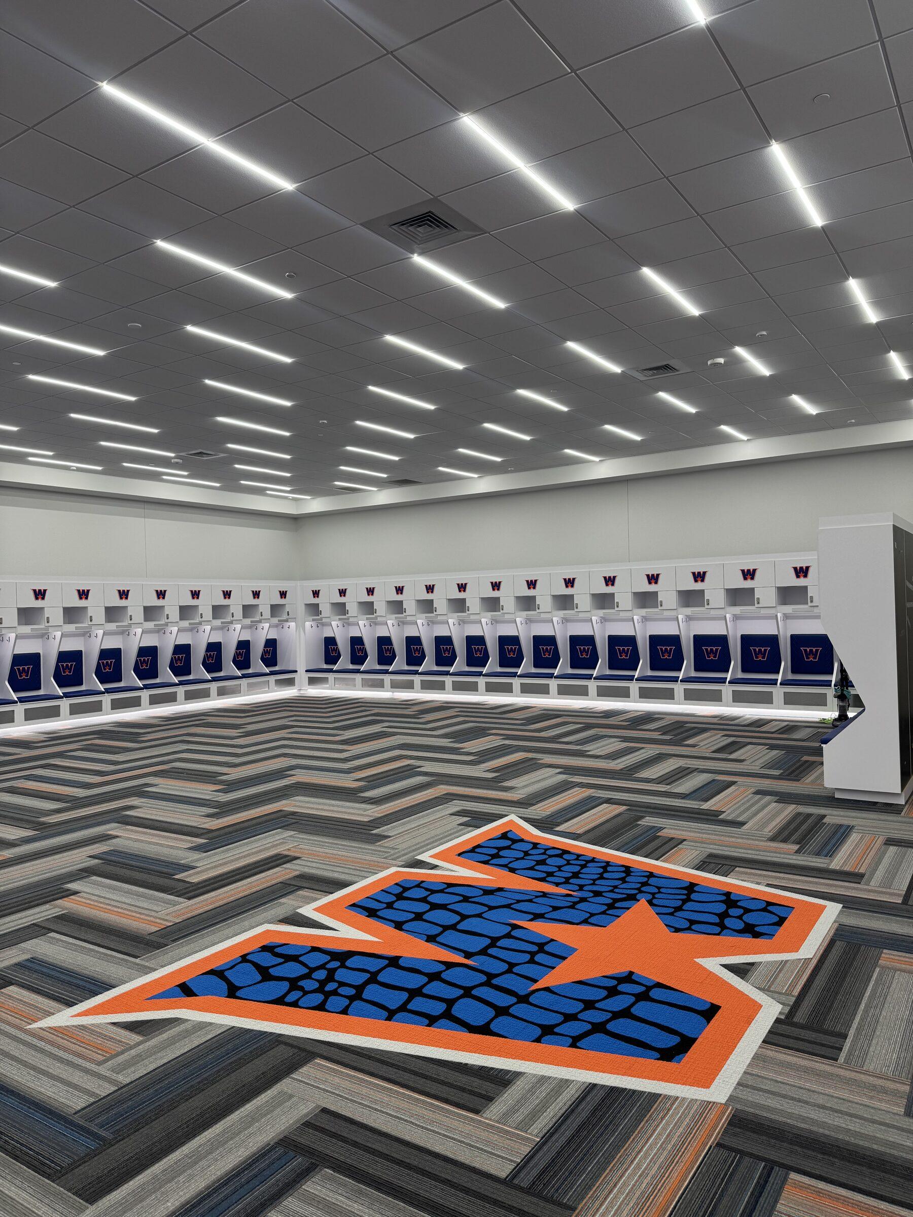 Huge sports-academy locker room with stadium lockers and logo carpet, freshly detailed