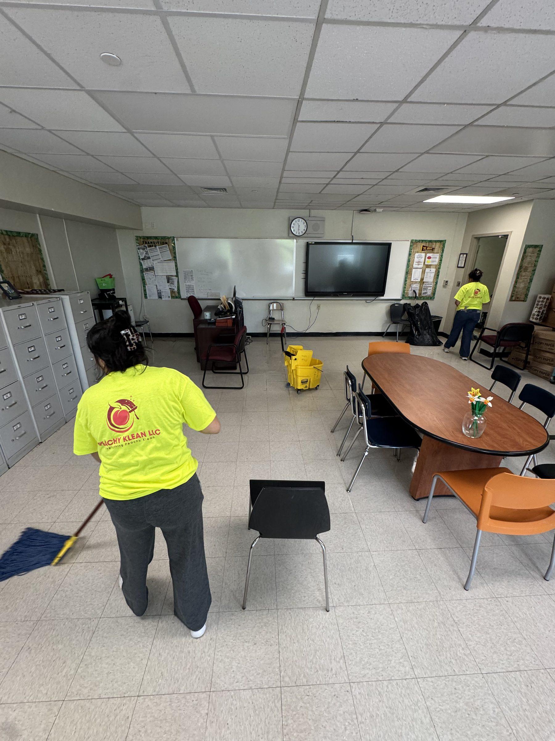 Peachy Klean crew members in branded high-vis shirts mopping a classroom-style office