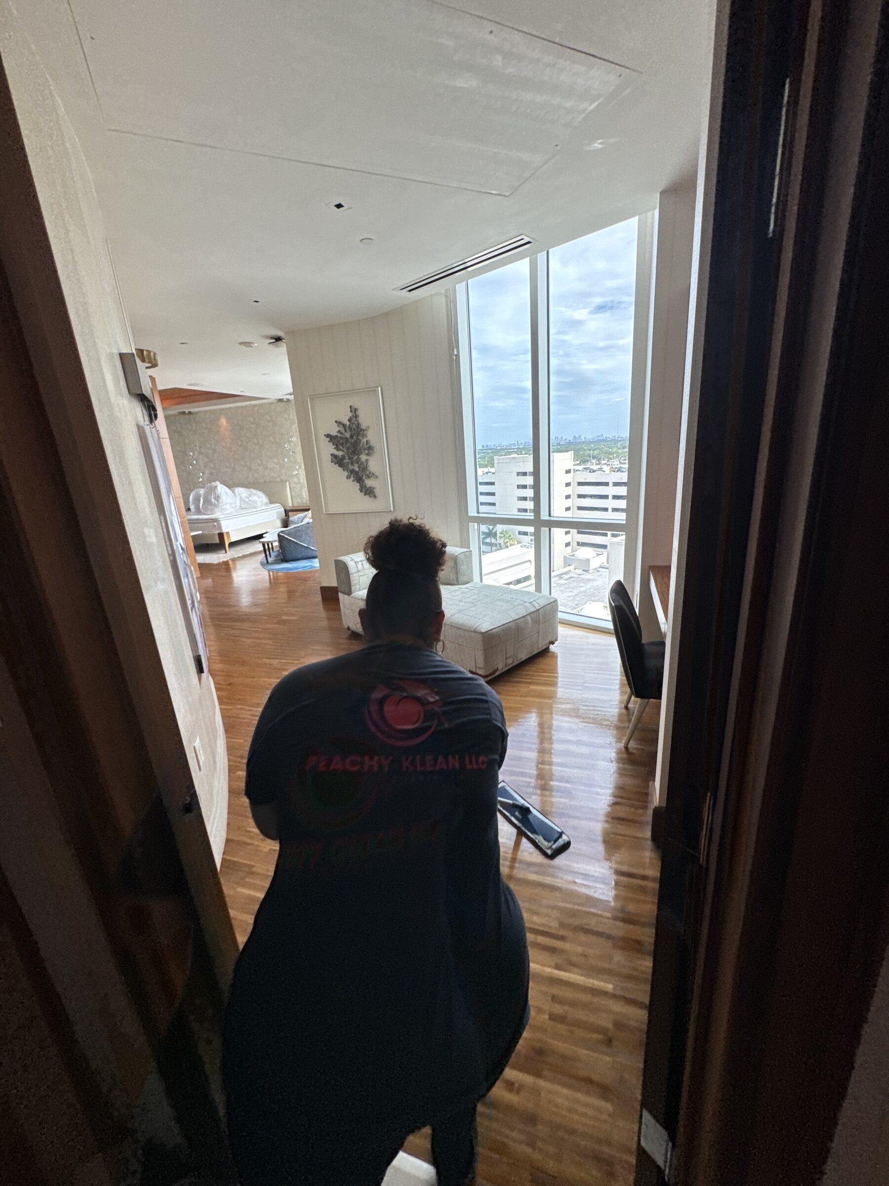 Crew member in a Peachy Klean uniform shirt detailing a suite with a spray bottle