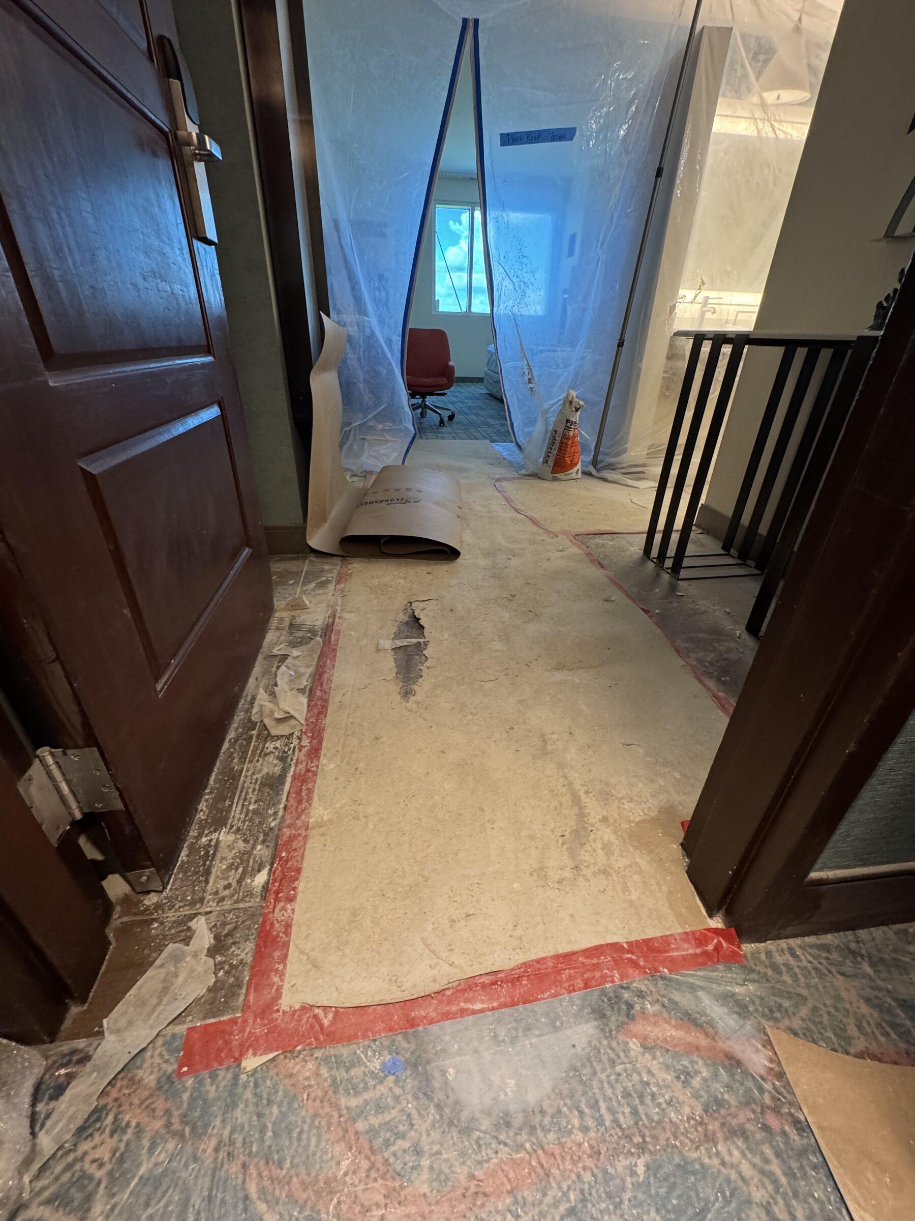 Hallway mid-renovation with torn-up carpet and containment plastic