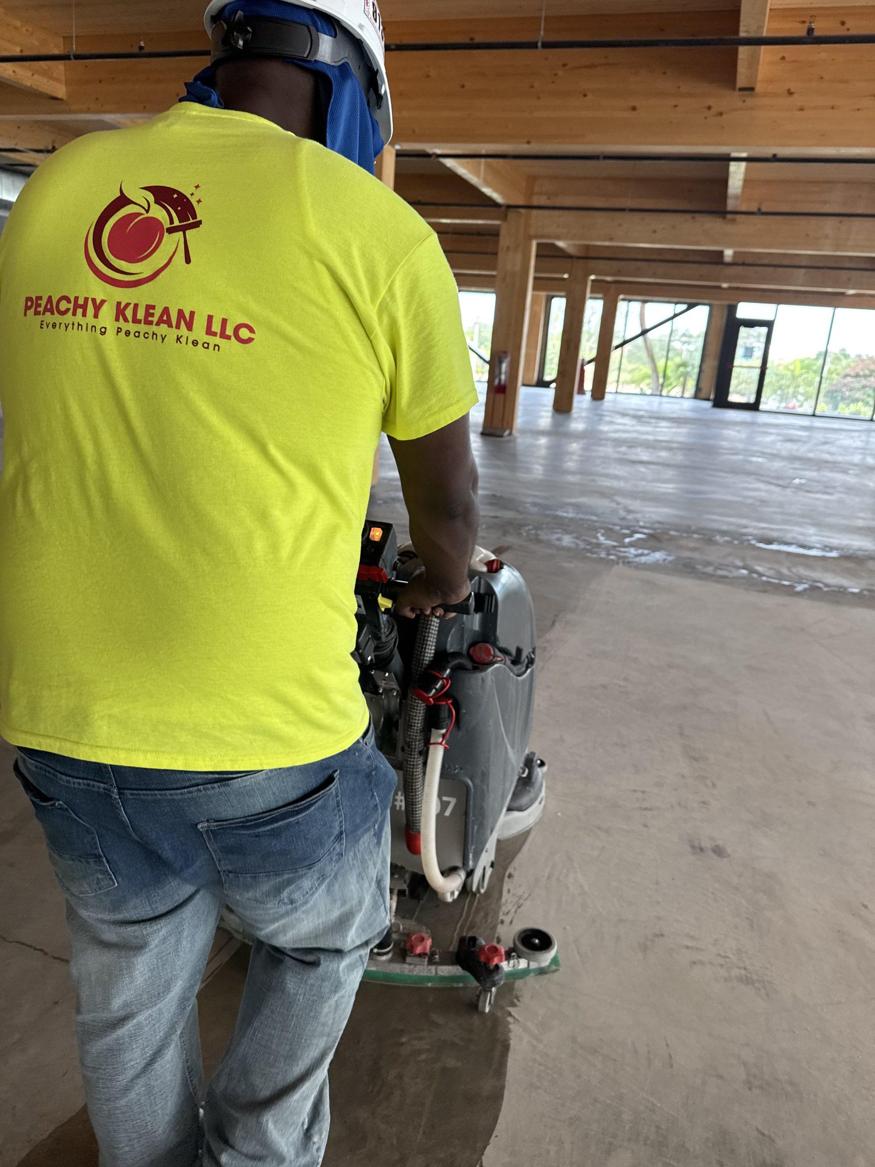 Peachy Klean crew member in a hard hat operating a walk-behind floor scrubber in a new timber-frame building