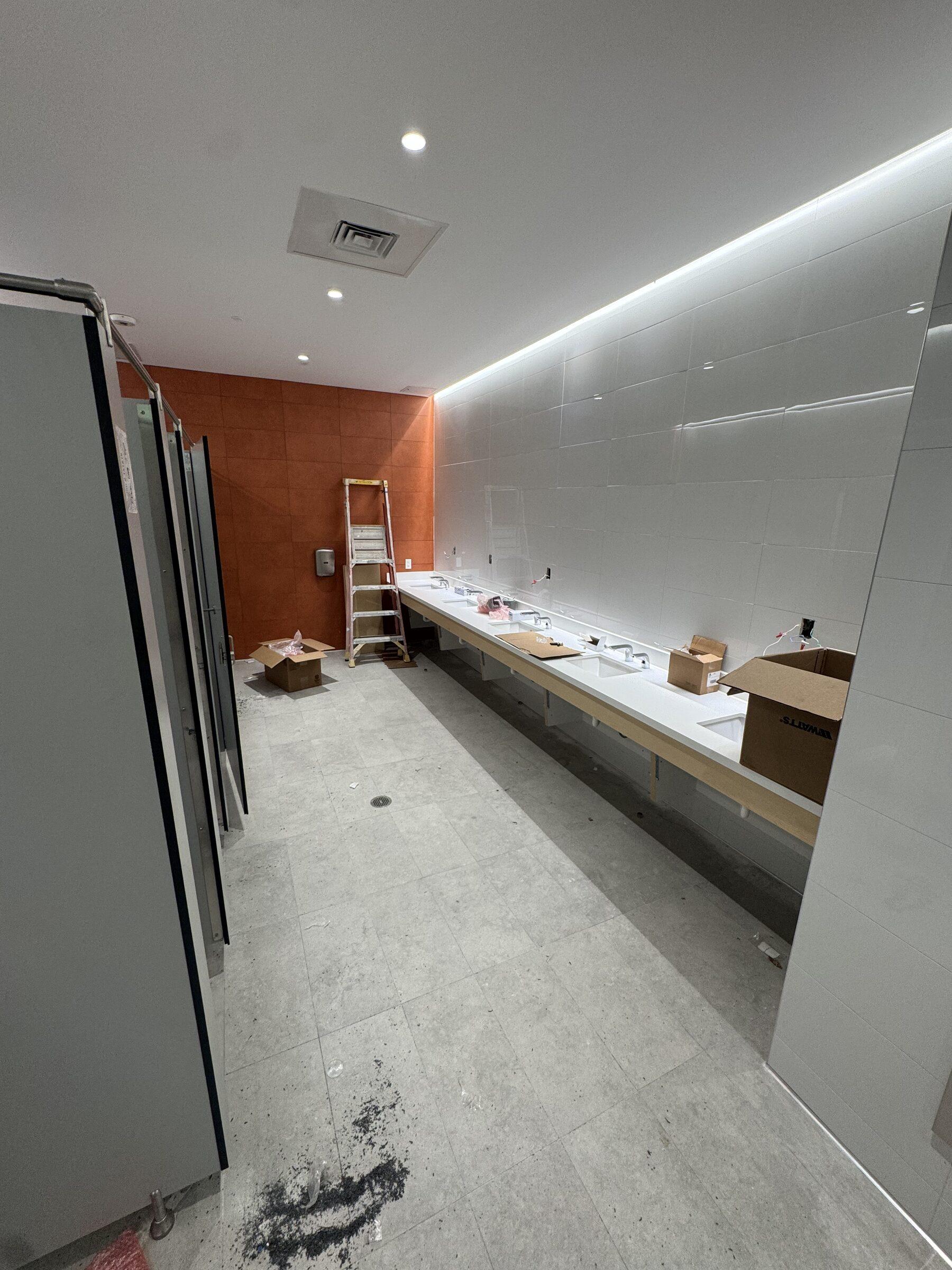 Restroom fit-out mid-build with ladder and materials, before final clean